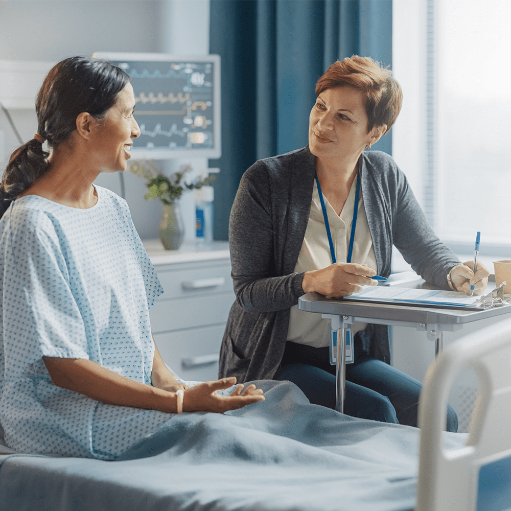 A patient in a hospital bed talking to a patient advocate