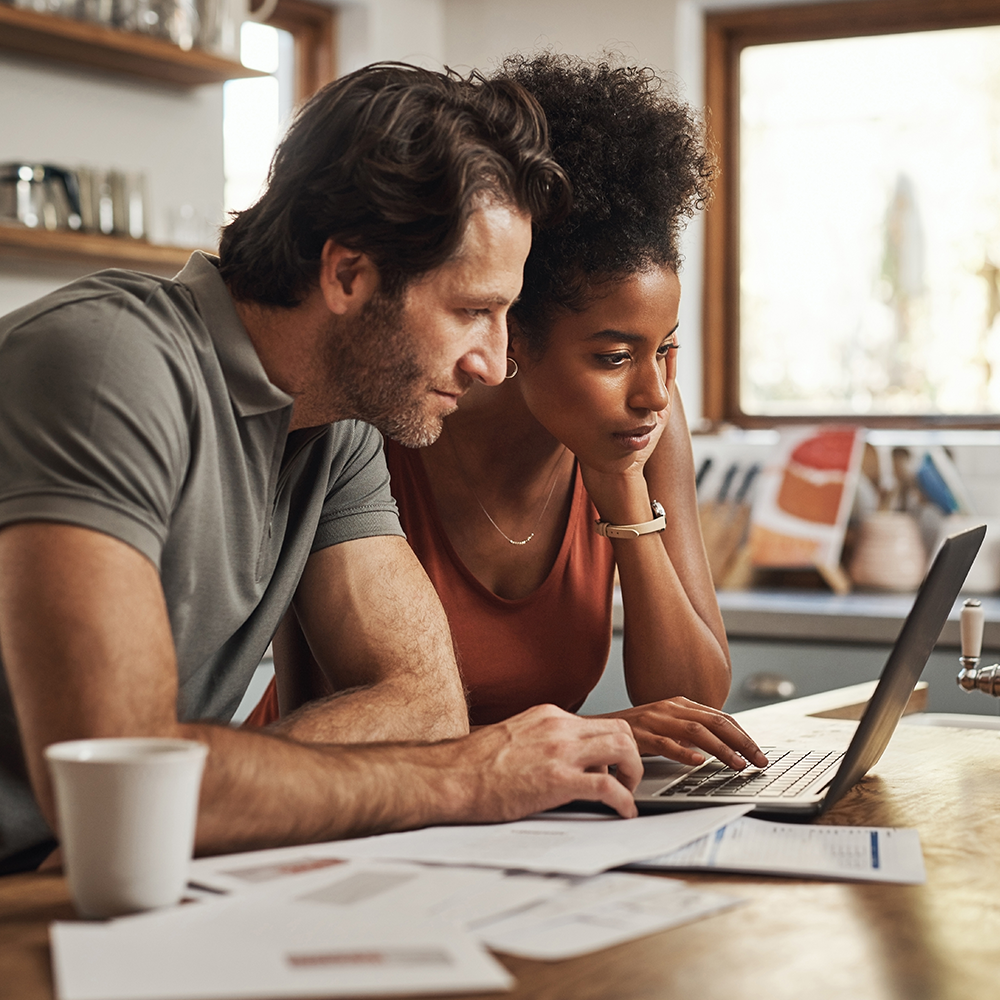 Two people at a kitchen table looking at a laptop screen